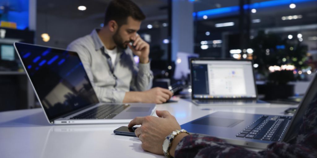 Professional in modern office calling on smartphone beside sleek laptop.
